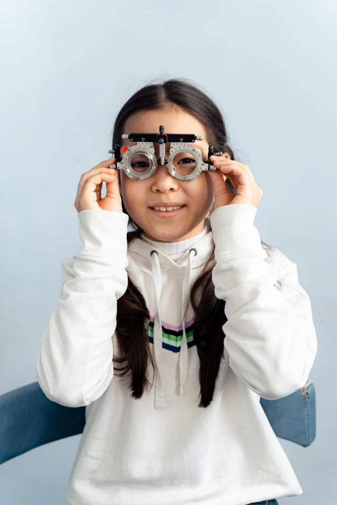 A young girl smiling while wearing an eye testing frame during a vision screening.
